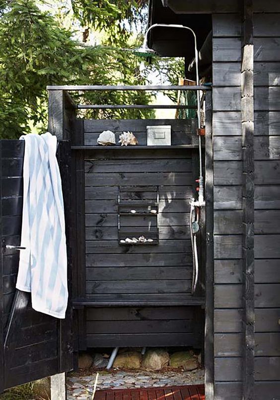 A weathered wood outdoor shower with shelves, sea inspired decor and stones on the ground