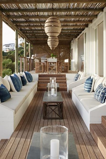 a welcoming beach patio with white benches, blue pillows, pendant wicker lamps and a dining set of wood