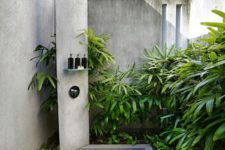 a welcoming outdoor shower with much greenery and a concrete shower zone with a stand