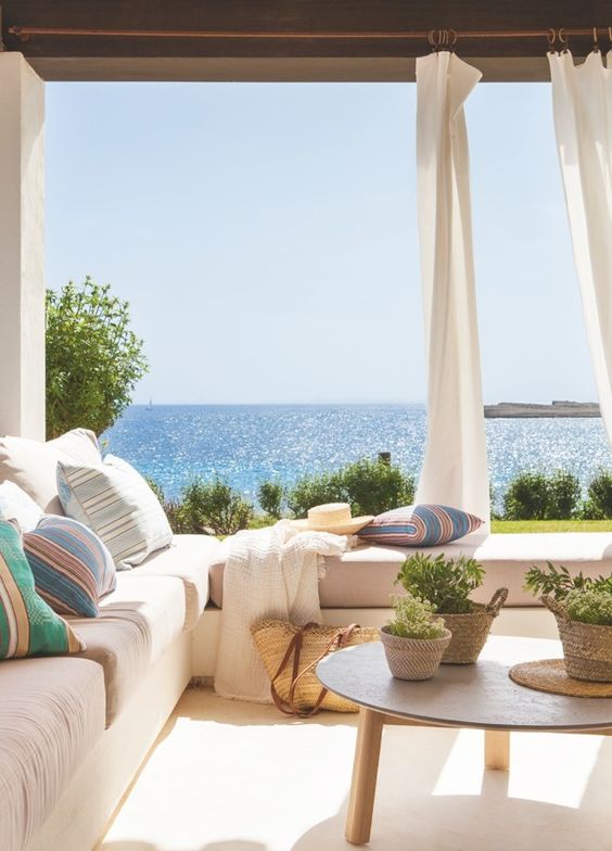 a welcoming seaside patio with a corner bench, potted greenery, baskets, colorful pillows and a fantastic view