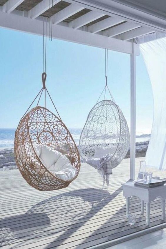 a white beach deck with a vintage stool, pendant wicker chairs and white textiles seems ethereal and chic