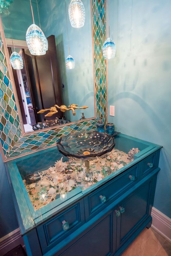 an electric blue vanity with a glass tabletop and seashells and pebbles under it plus jellyfish inspired pendant lamps