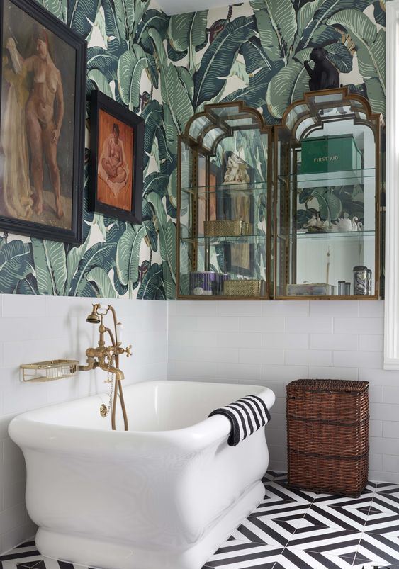 an elegant vintage tropical bathroom with banana leaf wallpaper, a catchy tub, glass and mirror cabinets and artworks