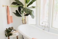an ethereal tropical bathroom with a vintage clawfoot tub, potted greenery and peachy pink textiles