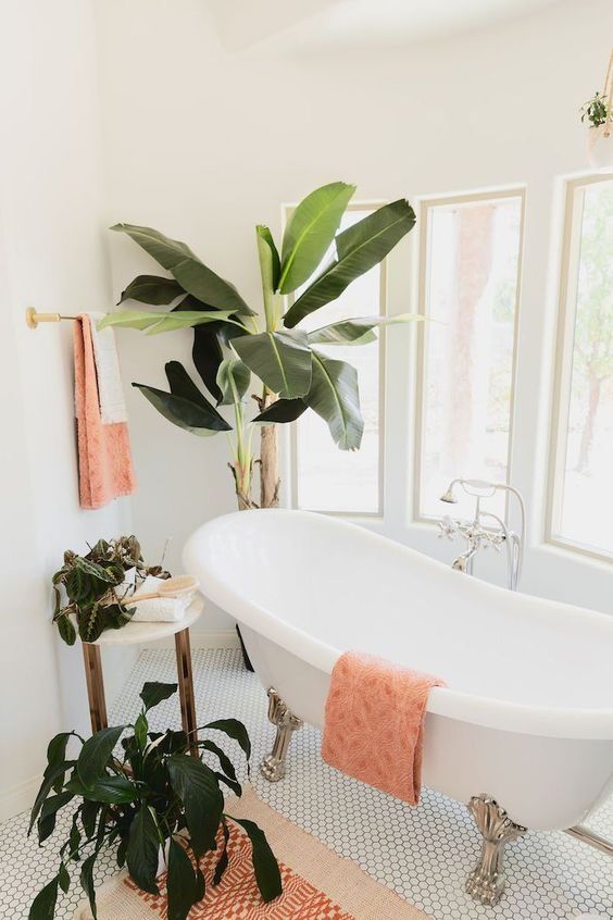 an ethereal tropical bathroom with a vintage clawfoot tub, potted greenery and peachy pink textiles