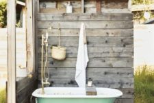 an outdoor rustic bathroom nook with weathered wood screens, a green tub, a pallet rug and some accessories