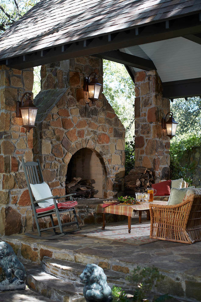 a rustic patio with a stone fireplace and pillars, rattan and wooden furniture and colorful textiles  (We Got Lites)