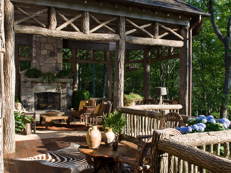 a rustic patio done with logs and a stone fireplace, wooden furniture, potted greenery and blooms  (William T Baker)
