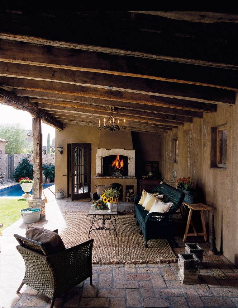 a rustic covered patio with wooden beams, painted wicker furniture and a fireplace looks like an outdoor living room  (Don Ziebell)
