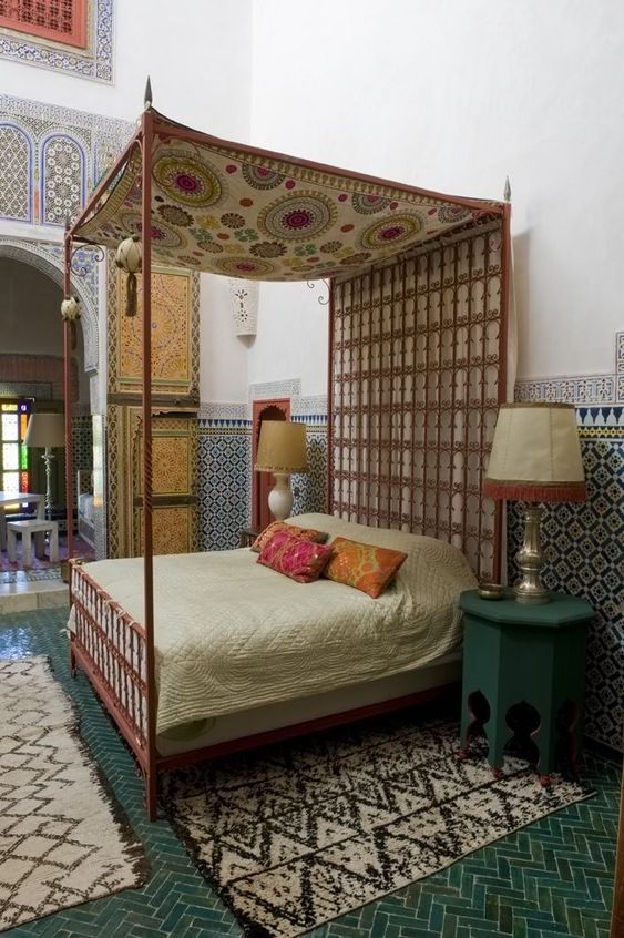 a Moroccan bedroom all clad with traditional tiles, with rugs, carved furniture and boho rugs and bedding