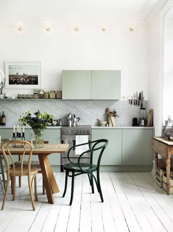 a Nordic kitchen with green cabinets, white stone countertops and a backsplash, a wooden table and vintage chairs