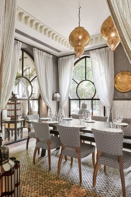 a beautiful Moroccan dining space done in neutrals, with grey walls, a long table with printed chairs, a patterned floor and metal pendant lamps