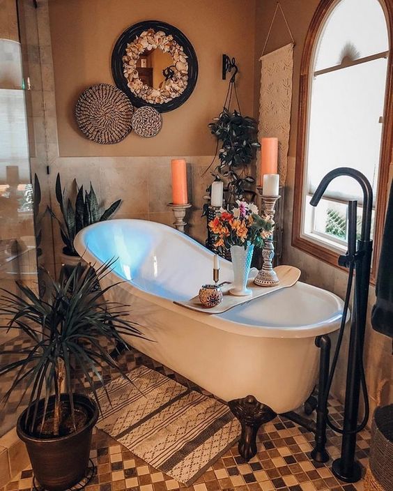 a boho bathroom with a clawfoot tub, candles, potted plants, decorative baskets and an ornate mirror