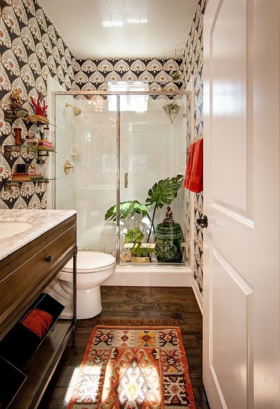 a boho meets art deco bathroom with catchy wallpaper, a boho rug, greenery and a painted side table
