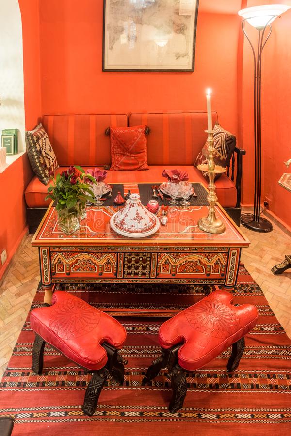 a bold red Moroccan dining space with red walls and furntiure, a carved and painted wooden table, a printed rug and a lovely lamp
