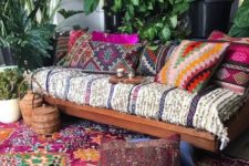 a bright boho patio with a wooden bench with printed and colorufl upholstery, bright pillows, potted greenery and baskets with lids