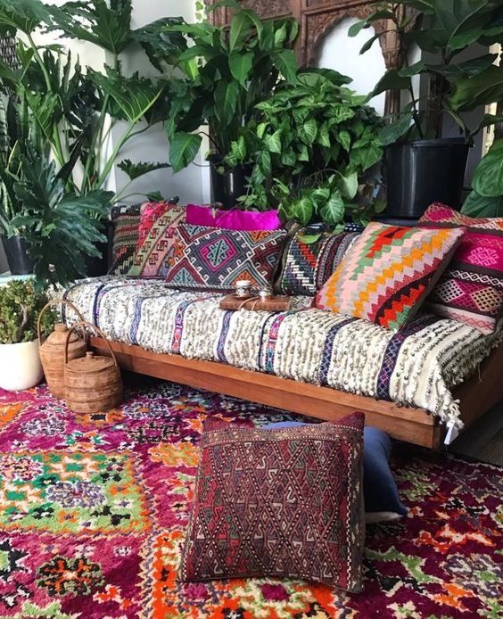 a bright boho patio with a wooden bench with printed and colorufl upholstery, bright pillows, potted greenery and baskets with lids