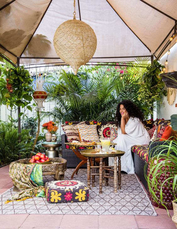 a bright boho patio with colorful pillows, tetiles, woven lamps and a wooden coffee table plus lots of greenery