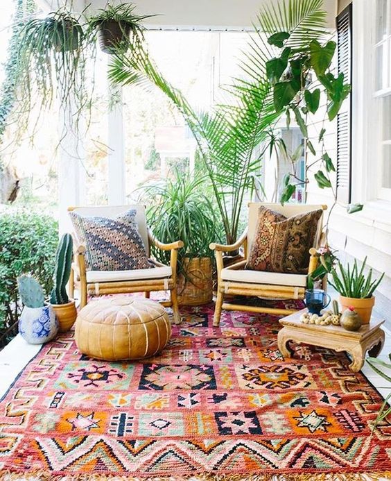 a bright boho patio with rattan furniture, a wooden low table, a leather ottoman, potted plants and cacti