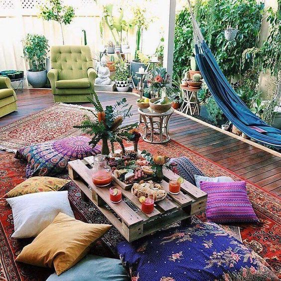 a bright boho space with a blue hammock, bright furniture and cushions, a pallet table and potted greenery