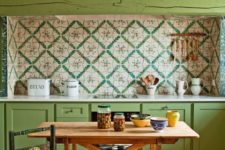 a bright boho vintage kitchen with green cabinets and a beam, a colorful tile backsplash and a bright mosaic floor