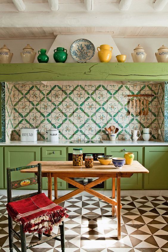 a bright boho vintage kitchen with green cabinets and a beam, a colorful tile backsplash and a bright mosaic floor