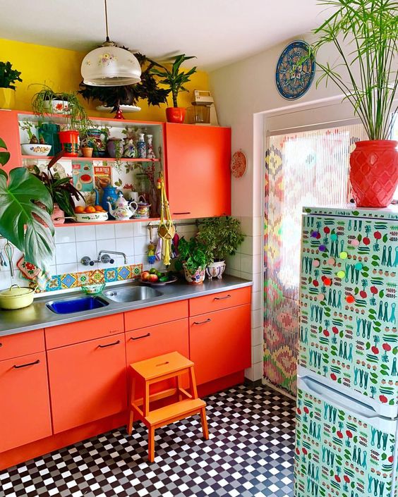 a bright orange kitchen with mustard walls, a tile backsplash and a printed fridge plus a printed curtain