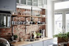 a chic Scandinavian kitchen with a brick wall, grey and frosted glas scabinets, butcherblock countertops and much light