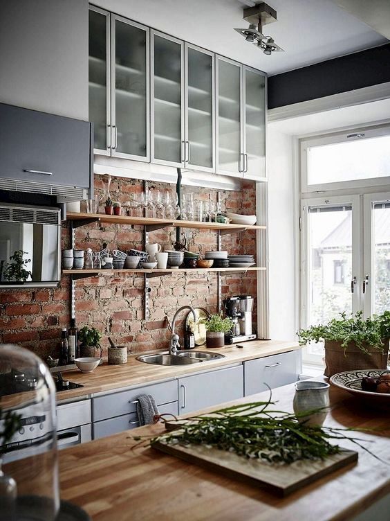 a chic Scandinavian kitchen with a brick wall, grey and frosted glas scabinets, butcherblock countertops and much light