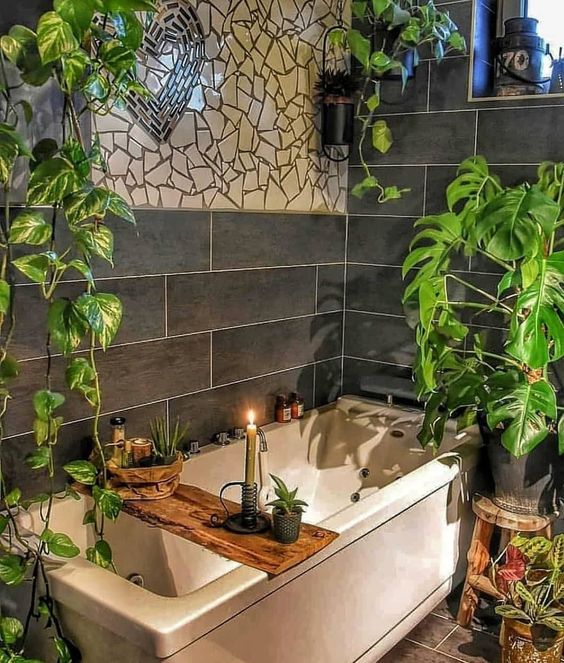 a chic boho bathroom with mosaics on the wall, potted greenery, a wooden caddy and candles