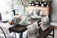 a chic farmhouse dining space with a wooden buffet, a dark stained wooden dining set, a metal lamp and lots of greenery