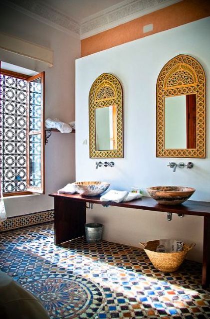 a colorful Moroccan bathroom with oranted mirrors, painted bowl sinks, a tiled floor and a cool window