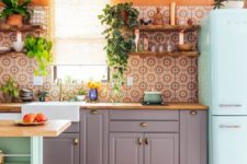a colorful boho kitchen with a bright orange wall, a mint fridge, grey cabinets with a wooden top and a printed tile backsplash