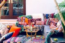 a colorful boho patio with bright pillows and ottomans plus rugs, a colorful canopy and a small gilded coffee table