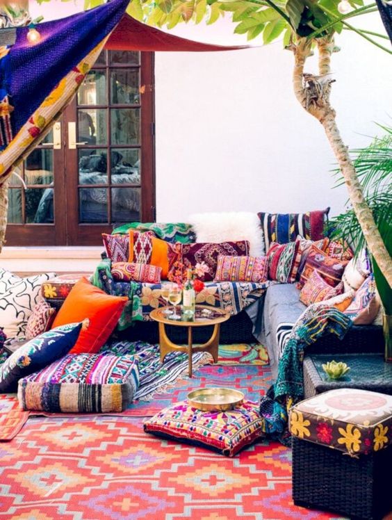 a colorful boho patio with bright pillows and ottomans plus rugs, a colorful canopy and a small gilded coffee table