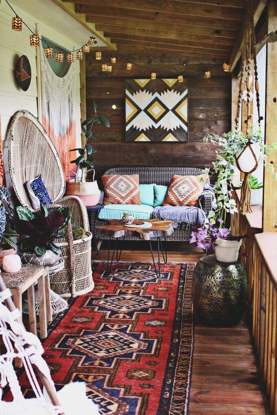 a colorful boho patio with wicker and wooden furniture, folksy artworks, lights, fringe, macrame and boho rugs