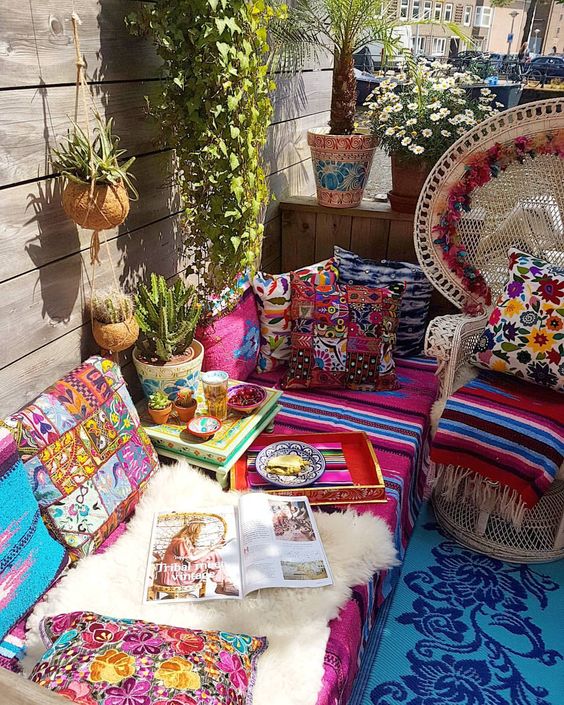a colorful boho patio with wicker furniture, printed and bright textiles, potted cacti and plants