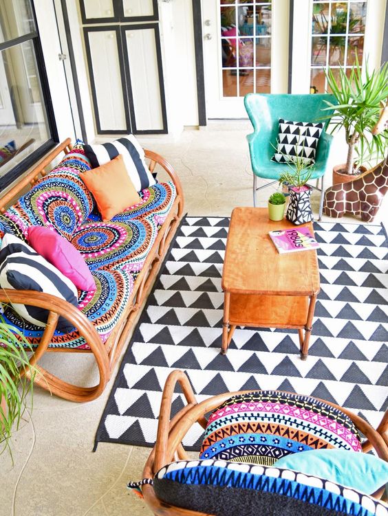 a colorful boho space with rattan furniture, colorful pillows and tetiles, a printed rug and potted plants