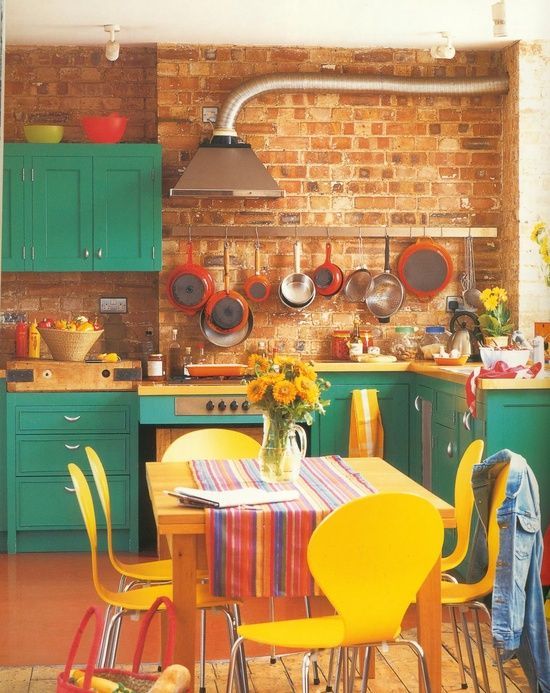 a colorful kitchen with emerald cabinets, yellow chairs, printed textiles and red pans and tableware