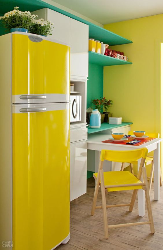 a colorful kitchen with white cabinets, a minty green storage unit, yellow chairs and a fridge plus more yellow touches