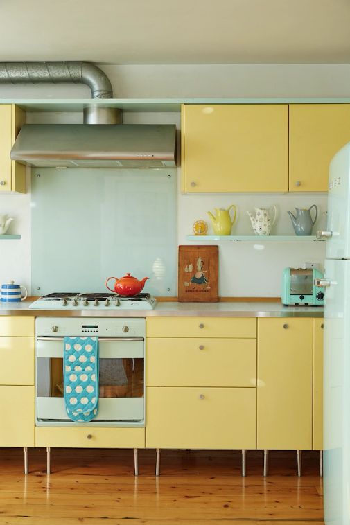 a colorful modern kitchen with yellow cabinets, a mint glass backsplash, a mint fridge and a cooker is fun