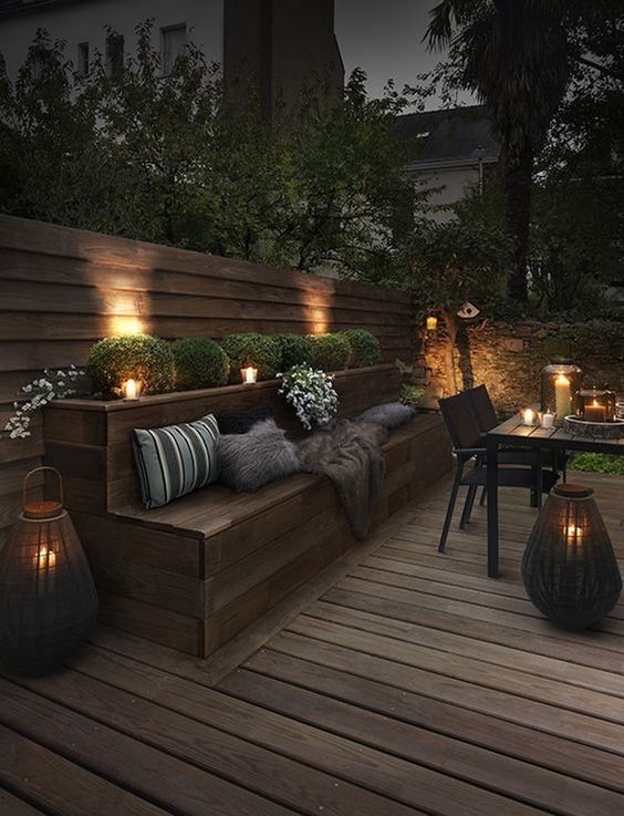 a contemporary meets rustic patio with wooden furniture, candle lanterns, boxwood and blooms