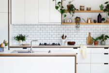 a contemporary white Nordic kitchen with sleek cabinets, wooden countertops, potted greenery and sa white subway tile backsplash