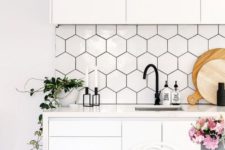 a contemporary white kitchen with sleek cabinets, hex tiles with black grout, black hardware and blooms