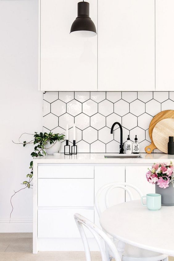 a contemporary white kitchen with sleek cabinets, hex tiles with black grout, black hardware and blooms
