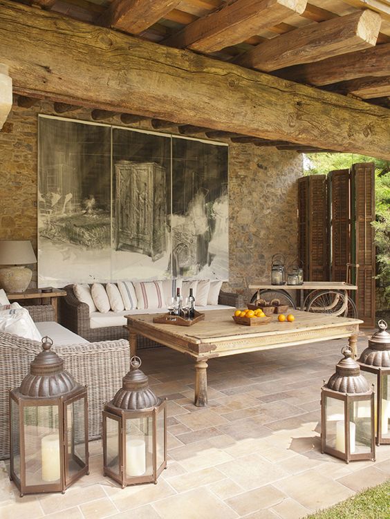 a countryside patio with wicker and wooden furniture, candle lanterns, an artwork and a shutter screen