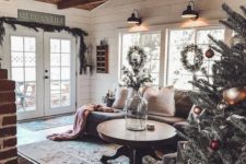 a cozy rustic living room with a round wooden table, a brick fireplace, a wooden ceiling with beams and an evergreen garland