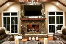 a cozy rustic living room with beams on the ceiling, a stone clad fireplace, a large leather sofa and candles