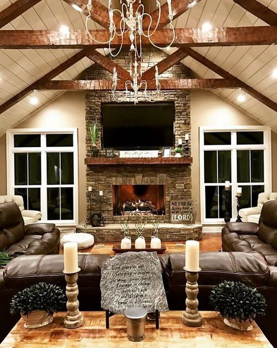 a cozy rustic living room with beams on the ceiling, a stone clad fireplace, a large leather sofa and candles