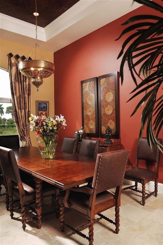 a dark dining space with a red accent wall, a dark heavy carved table, leather chairs and a metal Moroccan lamp that creates a mood